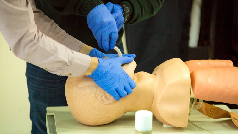 Two people in blue gloves practicing intubation on a medical mannequin, demonstrating airway management techniques.